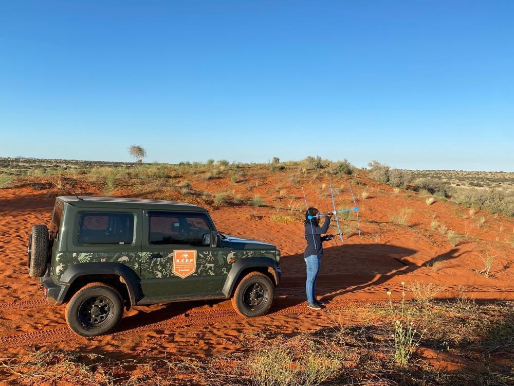 A student using tracking equipment next to an off-road vehicle in the Kalahari desert.